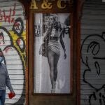 Imagen de archivo de un hombre caminando junto a unas persianas de un bar cerrado en el centro de Sevilla durante el mes de abril de 2020