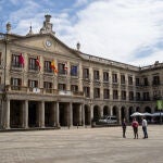 Varias personas observan desde la explanada las banderas a media asta y un crespón negro en la balconada del Ayuntamiento de Vitoria-Gasteiz