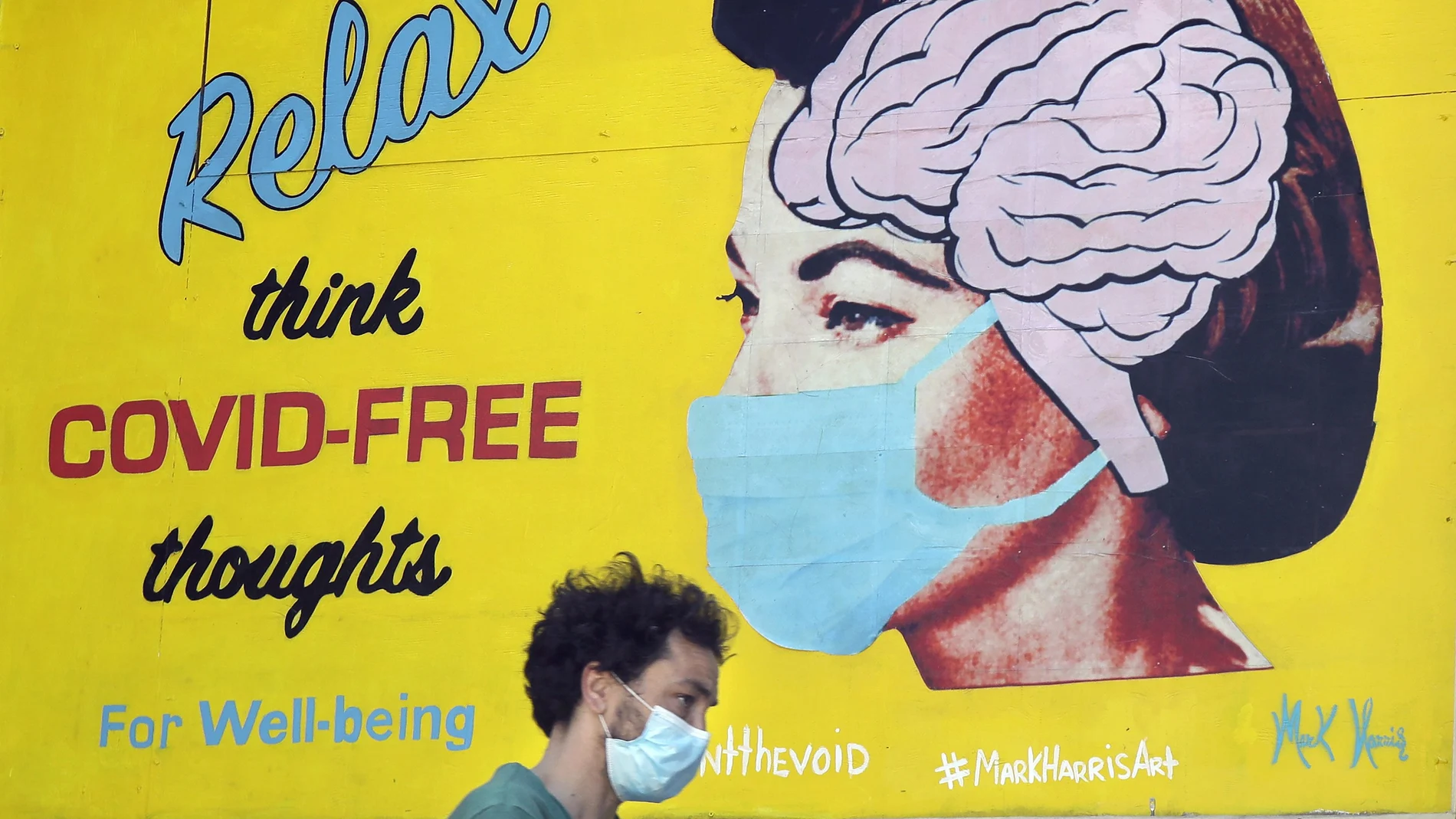 Un hombre con mascarilla pasa bajo un cartel que anima a tener pensamientos positivos ante la Covid-19 en San Francisco