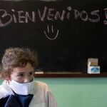 A girl wearing a face mask amid the new coronavirus pandemic attends class where the chalkboard reads in Spanish "Welcome!" at a rural school near Empalme Olmos, Uruguay, Monday, June 1, 2020. Some children returned to school Monday in some areas as Uruguay's total lockdown begins to ease. (AP Photo/Matilde Campodonico)