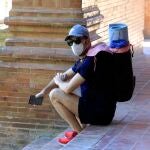Una persona, equipada con mascarilla, descansa sobre los escalones de la Plaza de España de Sevilla