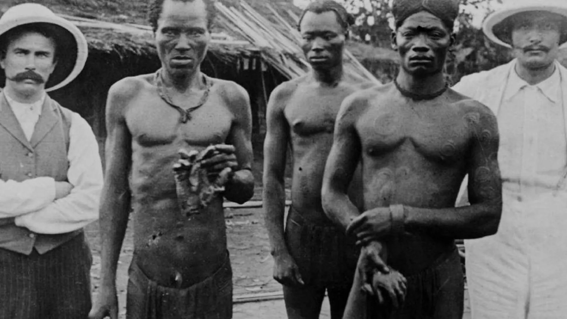 Dos esclavos sostienen unas manos amputadas ante la mirada impasible de dos agentes europeos. Una imagen tomada por Alice Seeley Harris en Baringa, Tshuapa, en mayo de 1904