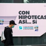 Un joven con mascarilla pasa por delante de un banco que anuncia una hipoteca