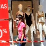 Una mujer pasea por la calle equipada con mascarilla a pleno sol