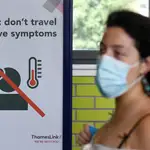 Una pasajera del metro de Londres con mascarilla, cruza ante un cartel que advierte de que no se use el transporte público si se tiene síntomas de la covid-19