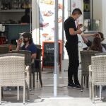 En la imagen, un camarero atiende a unos clientes en la terraza de un bar