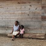 Duperat Laurette sits on a log with a girl at the entrance of a migrant shelter in Lajas Blancas, Darien province, Panama, Saturday, Aug. 29, 2020. The 45-year-old Haitian migrant and her husband emerged from the thick jungle that blankets the Panama-Colombia border here in Darien seven months earlier and have advanced no farther because of the new coronavirus pandemic. (AP Photo/Arnulfo Franco)