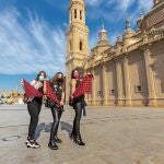 Tres mujeres zaragozanas posan este viernes en la plaza de El Pilar, con el cachirulo en la mano. El alcalde de Zaragoza, Jorge Azcón, ha emitido un bando para recordar que este año no hay Fiestas del Pilar y ha pedido a los ciudadanos que sean "solidarios", "conscientes", "responsables" y que eviten comportamientos que ayuden a la propagación de la pandemia.