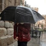 Una persona se protege de la lluvia en Ávila