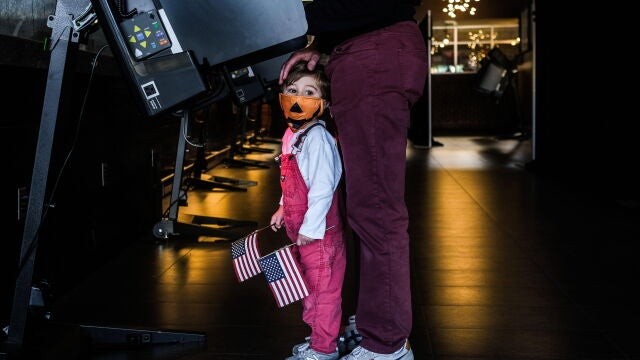 Un niño junto con dos banderas americanas acude a votar junto a su padre en Washington