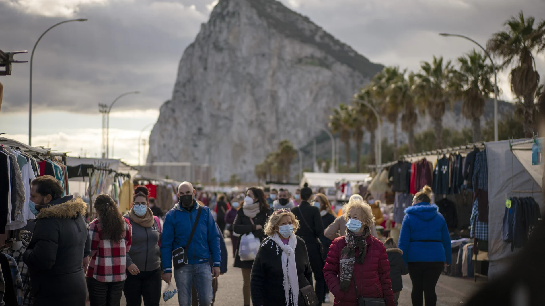 Backdropped by the Gibraltar rock, people walk along the stalls of a weekly market at the Spanish city of La Linea on Monday, Jan. 4, 2021. Fears of disruptions following Britain's departure from the European Union were replaced by coronavirus-related restrictions on border traffic between Spain and Gibraltar on Monday, the first working day at the United Kingdom's only land border with the European mainland. (AP Photo/Emilio Morenatti)