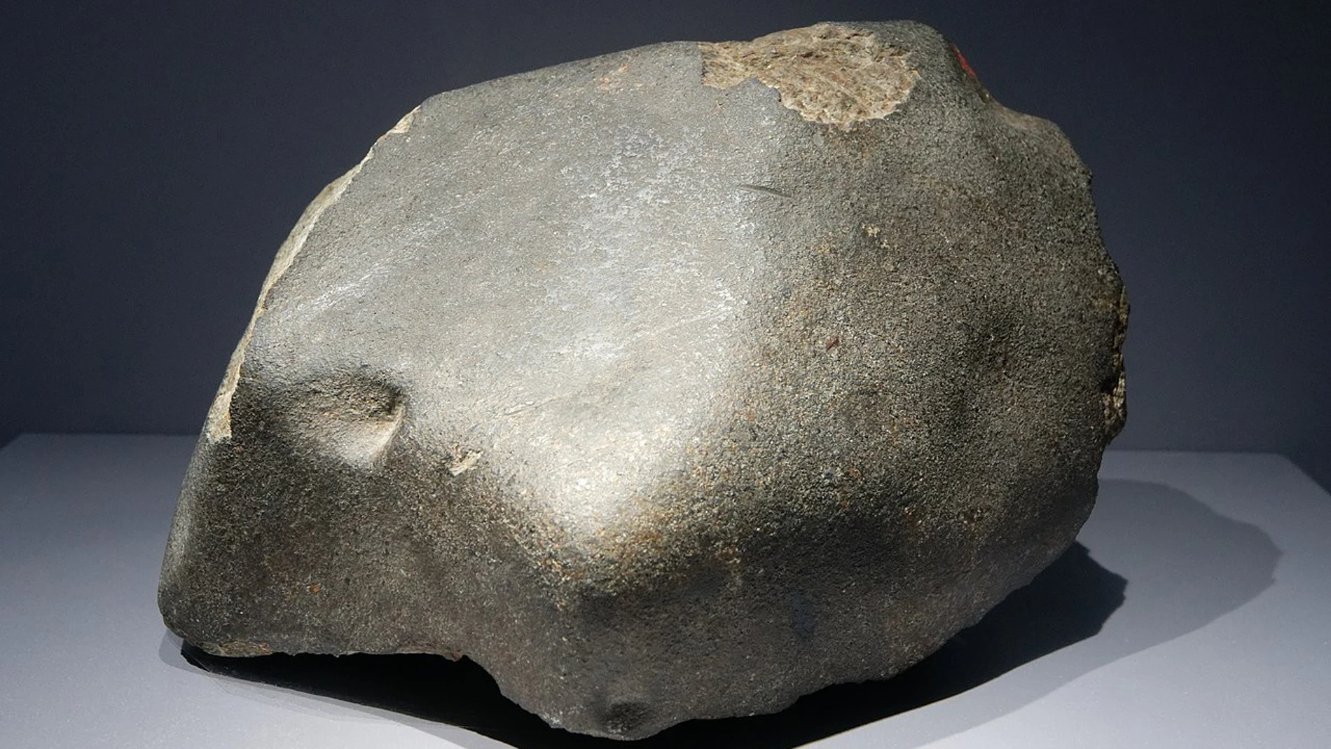 Una condrita ordinaria, el tipo de meteorito más común. Nótese la fina corteza de fusión y la matriz rocosa que asoma a través de ella.
