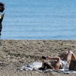 Un agente de policía indica a una mujer la obligatoriedad de la mascarilla también en la playa, como esta del Postiguet en Alicante
