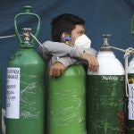A youth rests on his empty oxygen cylinder waiting for a refill shop to open in the San Juan de Lurigancho neighborhood of Lima, Peru, Monday, Feb. 22, 2021. A crisis over the supply of medical oxygen for coronavirus patients has struck in Africa and Latin America, where warnings went unheeded at the start of the pandemic and doctors say the shortage has led to unnecessary deaths. (AP Photo/Martin Mejia)