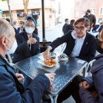 El candidato del PSC a la presidencia de la Generalitat, Salvador Illa (2d) acompañado del alcalde de Mollet del Vallès, Josep Monràs se toman unos churros tras su visita este sábado al mercado de la localidad, dentro de unas visitas territoriales a barrios con dificultades en Cataluña
