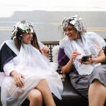 Dos mujeres sentadas en un banco fuera de una peluquería y sin mascarillas tras haber suspendido su obligatoriedad al aire libre