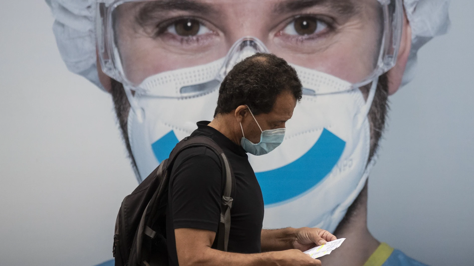 Un hombre camina debajo de un cartel que recomienda el uso de mascarillas por la Covid-19