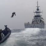 Un soldado de la Marina Real británica despega con una mochila propulsora desde una embarcación pequeña hasta otra grande