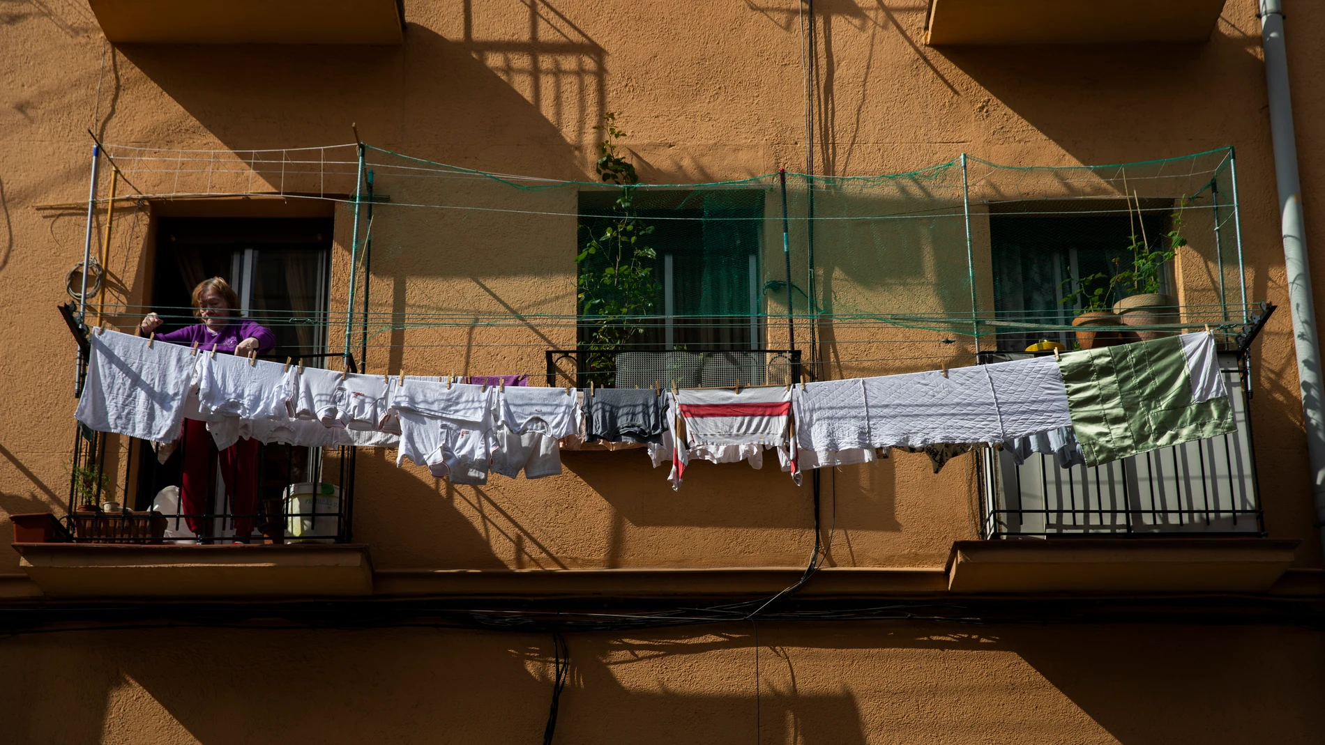 Imagen de una mujer tendiendo la ropa de la lavadora en el balcon de su casa en un edificio de Vallecas.