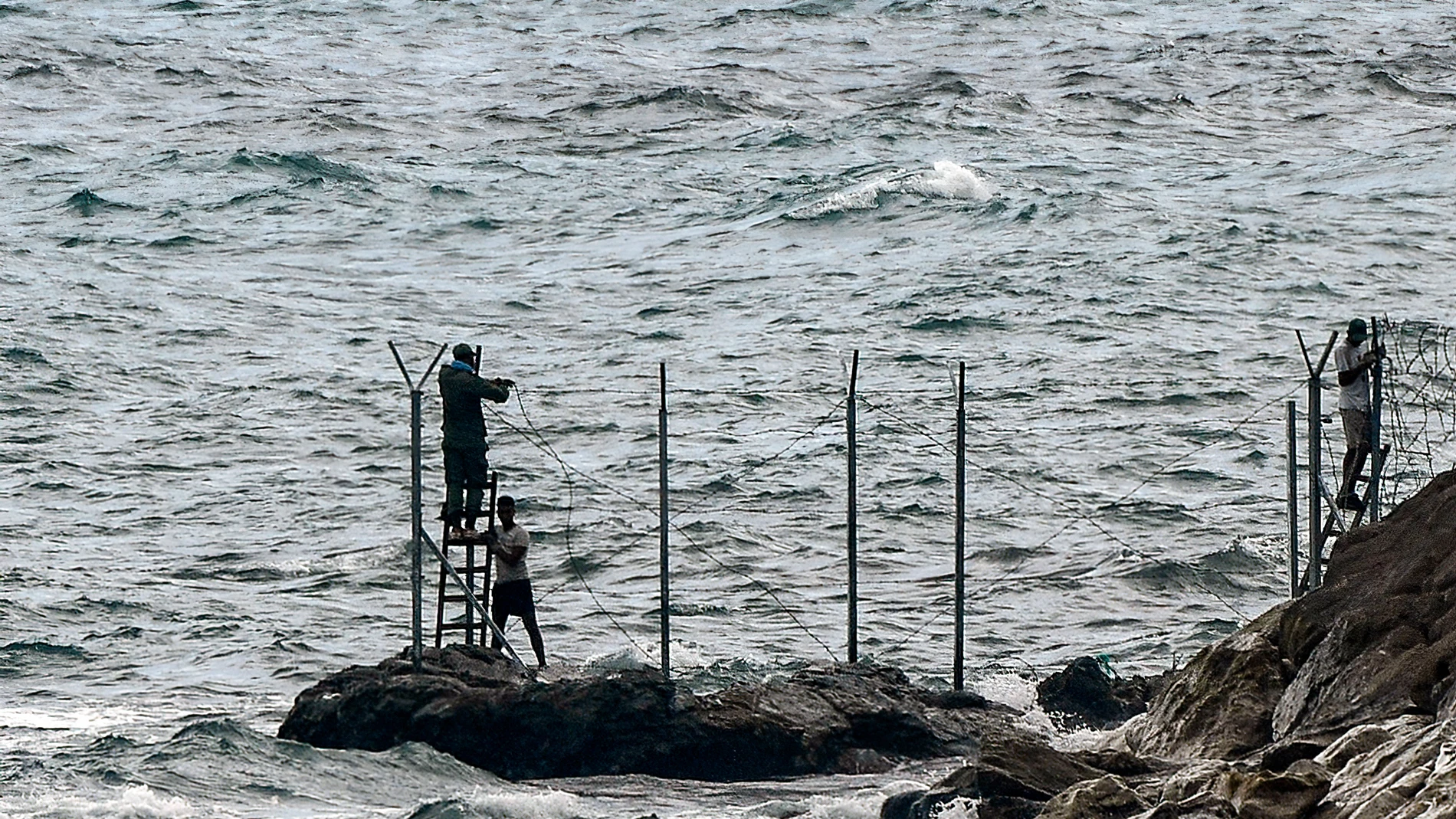 Personas (al fondo), instalan una valla en la playa del Tarajal, a 24 de junio de 2021, en Marruecos.