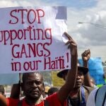 FILE - In this Dec. 10, 2020 file photo, a protester holds a sign with a message to stop supporting gangs during a protest demanding the resignation of then President Jovenel Moise in Port-au-Prince, Haiti. A UNICEF report says that escalating gang violence has displaced thousands of women and children in the capital in the first two weeks of June 2021. (AP Photo/Dieu Nalio Chery, File)
