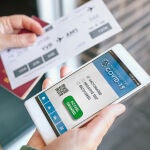 Una mujer sostiene su tel&eacute;fono con el certificado del pasaporte covid y la tarjeta de embarque