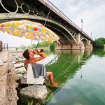 Un joven se refresca mientras pesca en la dársena del Guadalquivir de Sevilla durante una ola de calor 