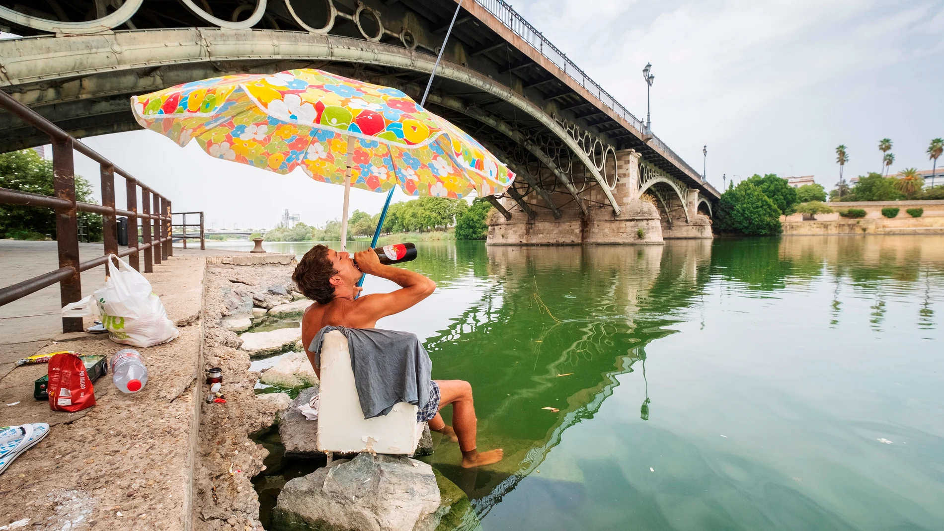 Un joven se refresca mientras pesca en la dársena del Guadalquivir de Sevilla durante una ola de calor