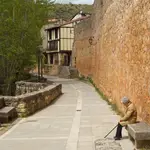 Una mujer descansa en un banco junto a las murallas de Covarrubias (Burgos)