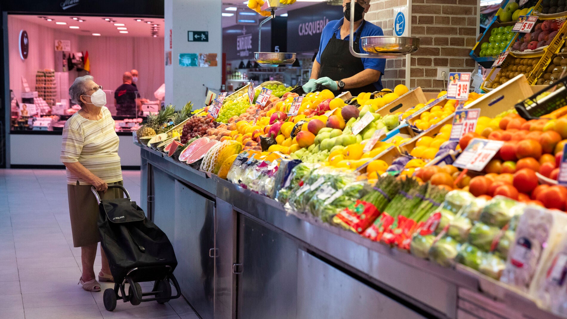 Imagen de una mujer mayor frente a una frutería.