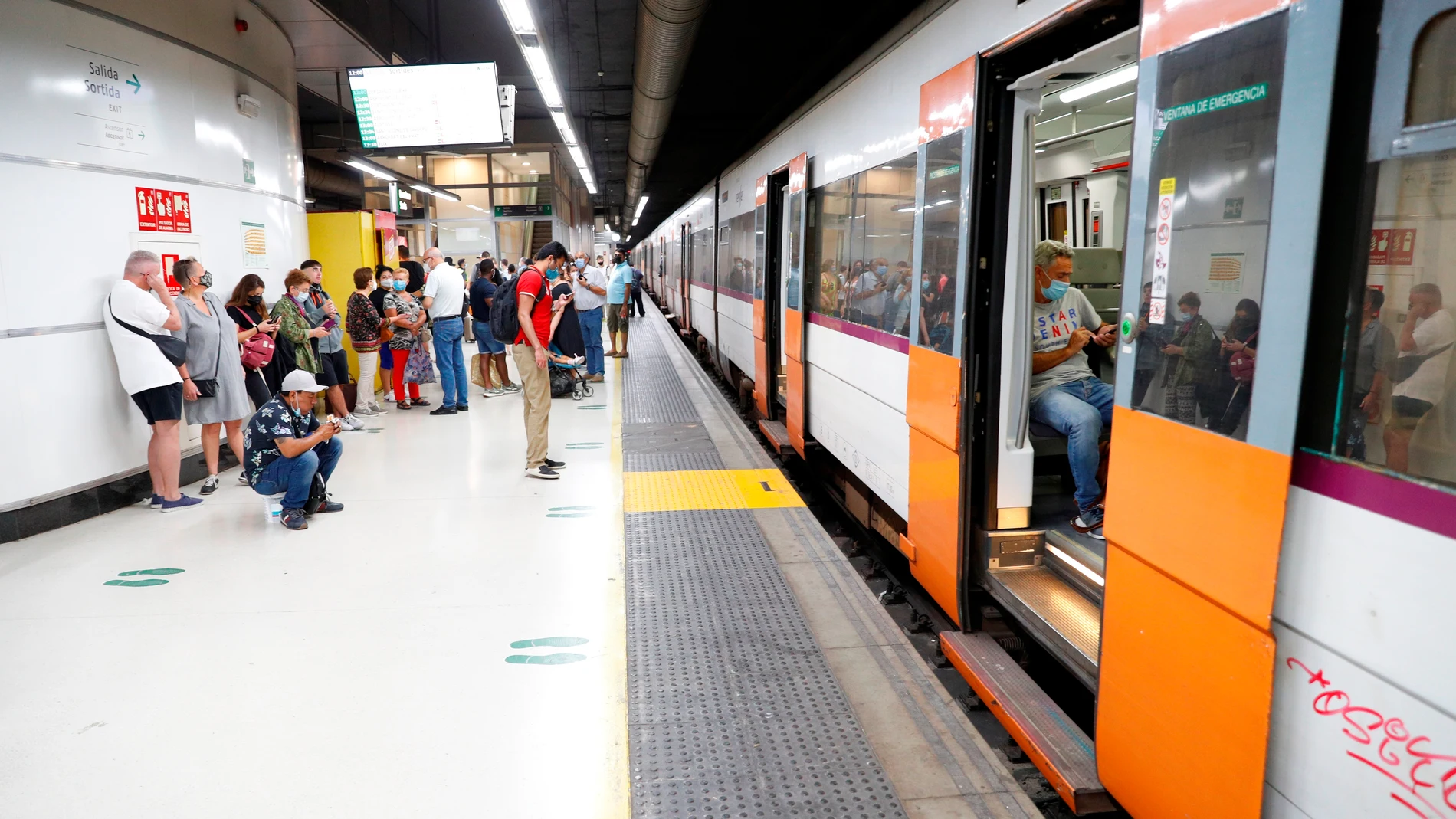 Varios pasajeros esperan ante un tren parado en Sants