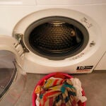 Un barreño con ropa sucia frente a una lavadora.