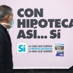 Gente con mascarillas pasando por delante de bancos que anuncian hipotecas