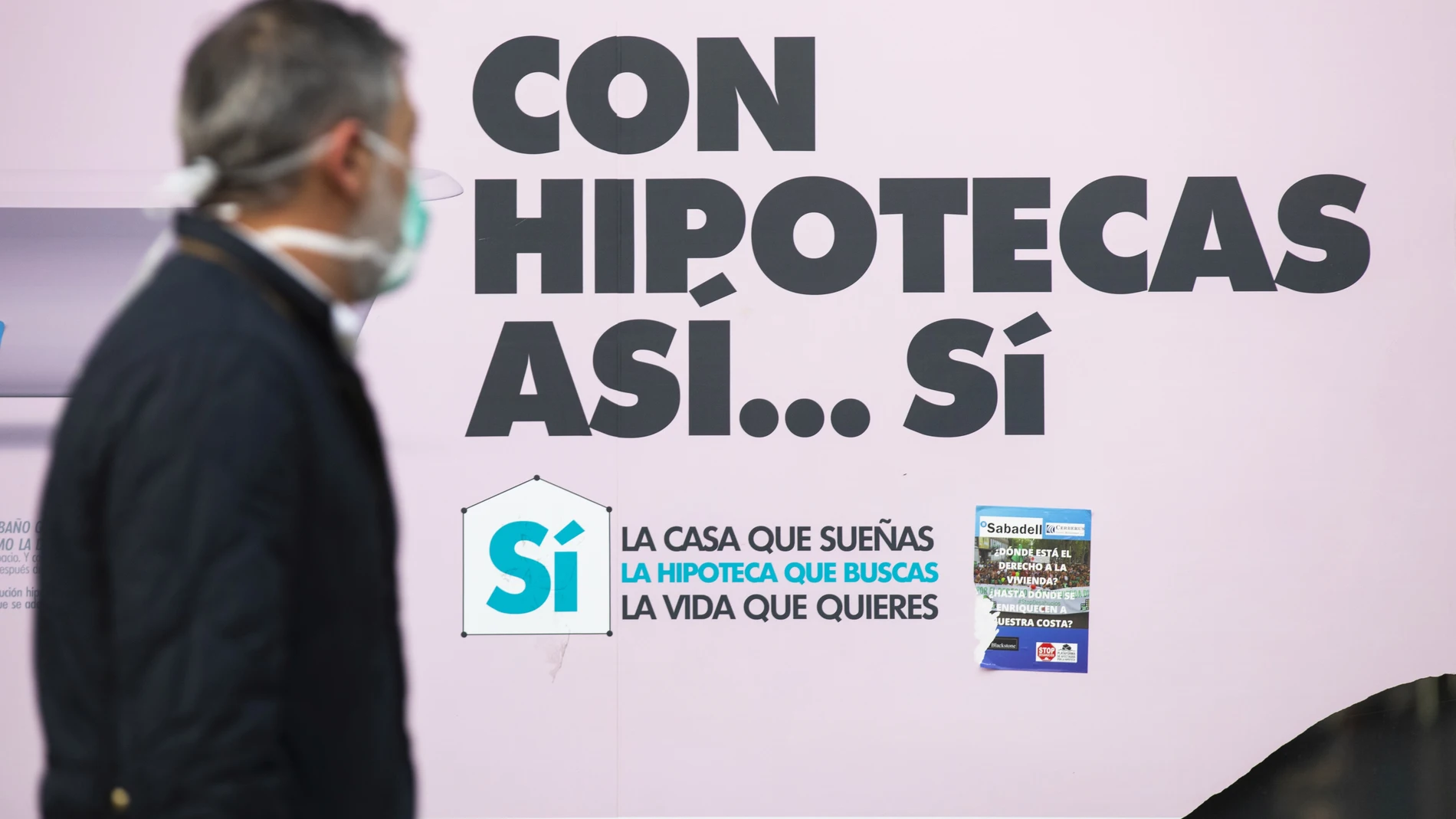 Gente con mascarillas pasando por delante de bancos que anuncian hipotecas