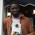 El novelista Mohamed Mbougar Sarr sostiene una copia de su libro en el balcón del restaurante parisino de Drouant