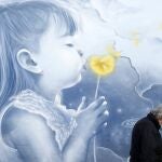 Un peatón con una máscara facial para protegerse contra el coronavirus, camina frente a un mural, en una estación de metro en Atenas, Grecia