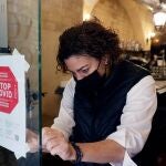 Una empleada de un hotel coloca un cartel a la entrada de su restaurante avisando de la obligatoriedad del pasaporte covid que entrará en vigor la noche del próximo viernes