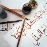 Obra de un estudiante de caligrafía árabe, utilizando bolígrafos de bambú y tinta marrón, trazando sobre la obra del profesor con tinta negra.