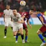El delantero del Sevilla Lucas Ocampos (i) escapa de Abdessamad Ezzalzouli (c) y Jordi Alba (d), ambos del FC Barcelona, durante el partido de LaLiga en Primera División que disputan este martes en el estadio Sánchez-Pizjuán, en Sevilla.
