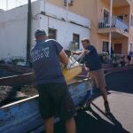 Dos hombres limpian de ceniza volcánica el frente de una vivienda en el municipio palmero de Tazacorte