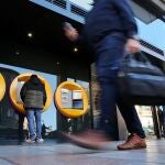 Varias personas hacen cola para entrar en una sucursal bancaria mientras otra opera en un cajero automático