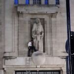 A man, after climbing a ladder, stands next to the statue of Prospero and Ariel from Shakespeare's play The Tempest by the sculptor Eric Gill outside the BBC's Broadcasting House in central London, Wednesday Jan. 12, 2022. British police have cordoned off an area outside the BBC in central London after a man was spotted scaling the building and using a hammer to attack a statue by controversial sculptor Eric Gill.