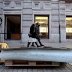Dos personas pasan junto al cristal roto y ante la tienda Apple ubicada en la calle Colón, en pleno centro de València