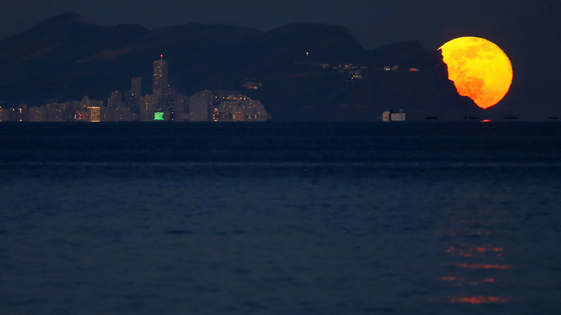 La primera luna llena del 2022 es vista desde la playa de San Juan a su salida por Benidorm.
