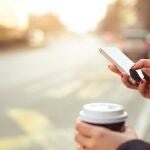 Una persona mira su móvil mientras toma un café