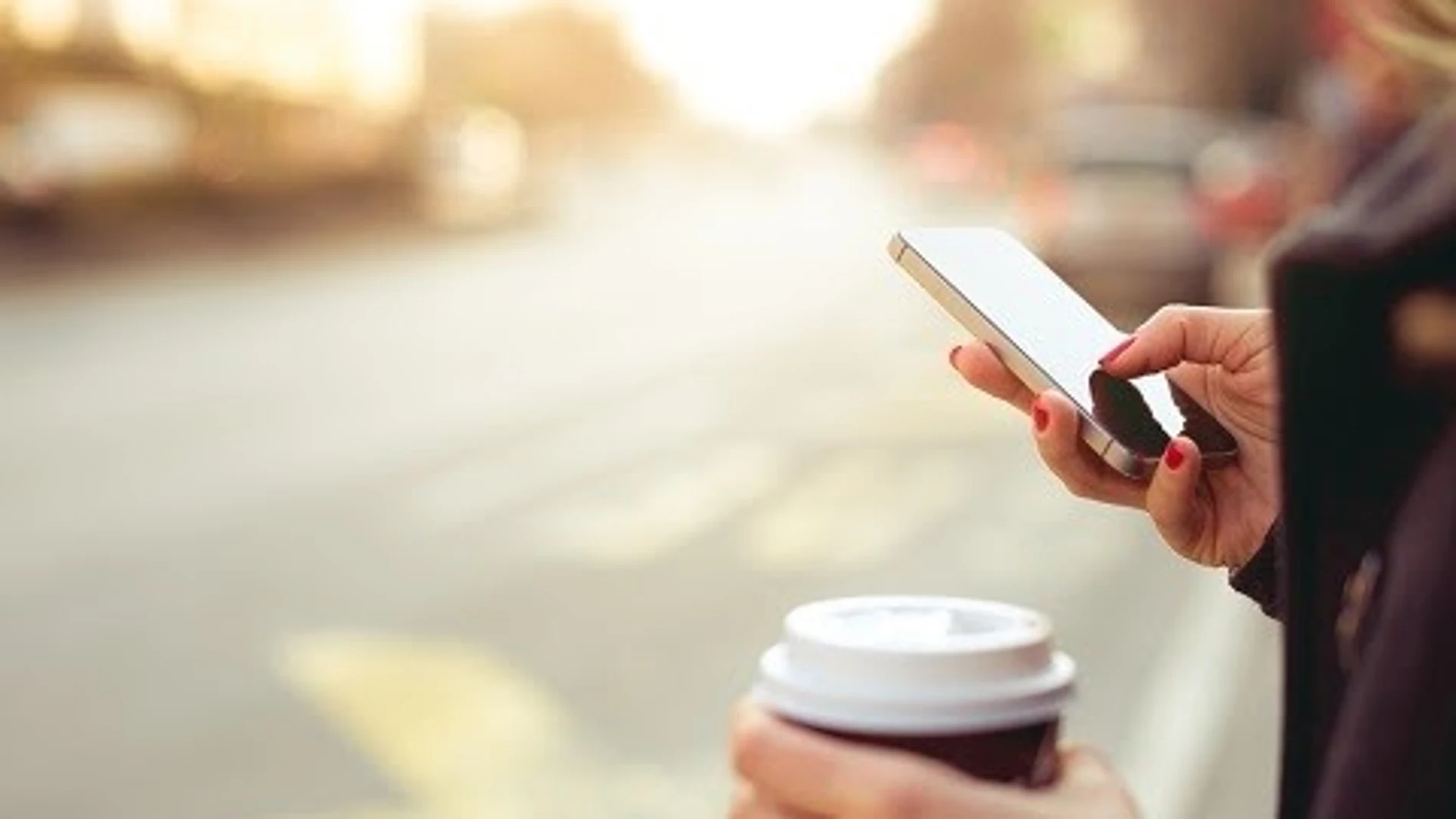 Una persona mira su móvil mientras toma un café