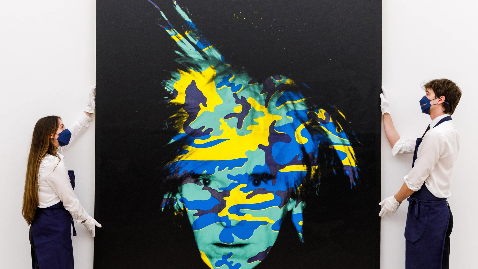 Fotografía cedida por Sotheby's donde aparecen dos empleados de esta casa de subastas mientras cuelgan la obra 'Autorretrato' de Andy Warhol, con un valor entre 15 y 20 millones y ejecutada en 1986, solo nueve meses antes de su muerte. EFE/ Sotheby's