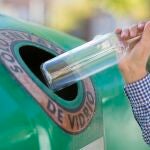 Un usuario deposita una botella de vidrio en un contenedor verde