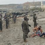 Miembros del Ejército observan a un grupo de inmigrantes que ha llegado a nado en los espigones fronterizos de Ceuta en una avalancha de inmigrantes sin precedentes en España