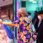 Imagen de una mujer mayor frente a una frutería junto a su carro de la compra.